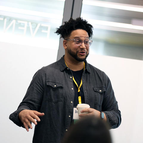 A man speaks and gestures in front of a group of people
