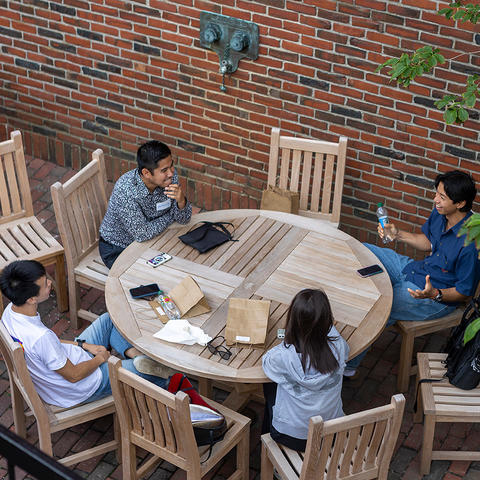 Students sit at a table outside and collaborate