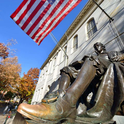 The John Harvard statue on a bright sunny day in Harvard Yard